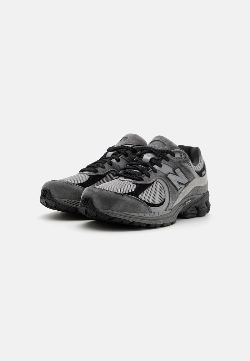 Une paire de baskets de sport grises et noires avec des détails en maille et en daim, des lacets noirs et des semelles noires rembourrées sur un fond blanc.
