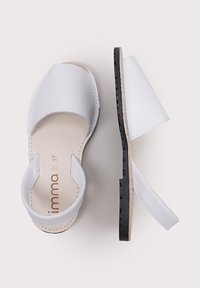 Sandalias de cuero blanco con un diseño simple, parte trasera abierta y suela de goma negra. Presenta una plantilla plana y detalles de costura mínimos.