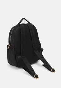 Mochila de tela negra con cremalleras doradas, correas acolchadas y un asa superior. Presenta una forma redondeada y bolsillos laterales. Textura suave.
