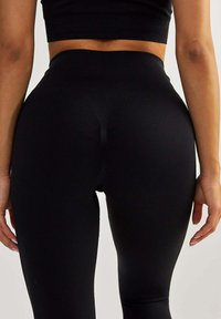 Schwarze hochtaillierte Leggings aus einem glatten, dehnbaren Stoff. Verfügt über ein nahtloses Design und konturierte Nähte entlang der Rückseite.