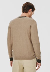 Sweter dzianinowy w jasnobrązowym kolorze z ciemnozielonym dekoltem. Posiada długie rękawy oraz ściągacze na mankietach i dolnym brzegu. Miękka faktura, luźny krój.