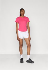 Tricou sportiv roz cu mânecă scurtă, pantaloni scurți albi, pantofi sport negri și șosete albe cu logo-ul Nike. Material neted, croială lejeră și design modern.
