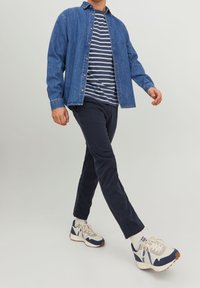Denim shirt over navy striped T-shirt, paired with navy pants and beige/blue sneakers. Focus on casual design and color contrast.