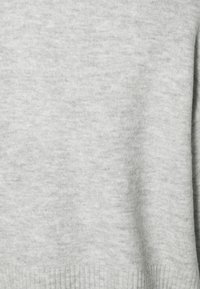 Suéter de punto gris claro con una textura suave, que presenta un dobladillo y puños acanalados, una superficie lisa y un diseño minimalista.