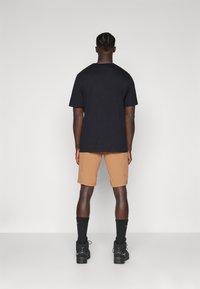 Svart bomull t-shirt, beige shorts, svarta strumpor och svarta skor, sedd bakifrån mot en neutral bakgrund. Korta ärmar, avslappnad passform.