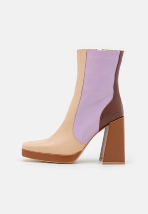 Enkelhoge laars met blokhak, beige voorkant, lavendelkleurig middenpaneel, donkerbruine achterkant en dikke bruine zool tegen een witte achtergrond.