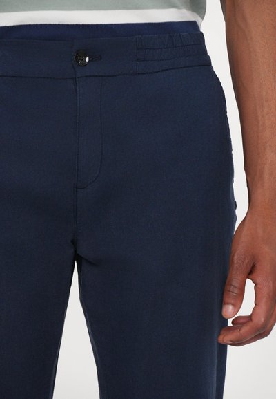 Marinblå bukser med en glat tekstur, som har elastisk talje, knaplukning og et slankt fit-design med sidelommer.