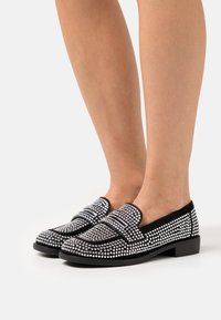Mocassins noirs ornés de strass en argent, avec un dessus lisse, un talon bas et un design classique avec deux bandes décoratives.