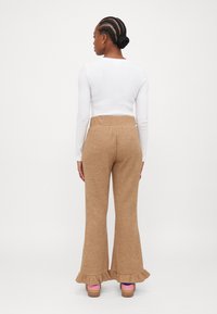 Beige knitted flared trousers with a ruffled hem, paired with wooden platform shoes. The outfit features a white long-sleeve top.