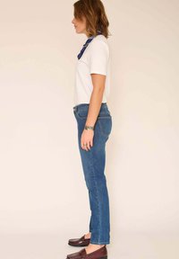 Jean skinny bleu à taille moyenne, associé à un t-shirt blanc uni et une écharpe marine. Texture denim lisse ; design décontracté.