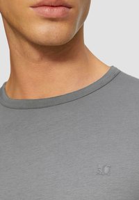 Graues Baumwoll-T-Shirt mit Rundhalsausschnitt, das ein dezentes Logo auf der Brust sowie eine glatte, leichte Textur aufweist.