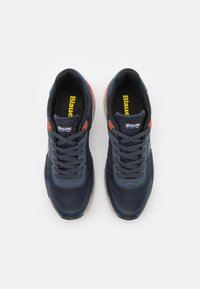 Marineblaue Sneakers mit einem Obermaterial aus Mesh und Synthetik, ausgestattet mit grauen Schnürsenkeln, roten Akzenten und einer beigefarbenen Gummisohle mit strukturierten Mustern.