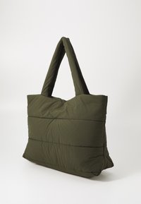 Sac fourre-tout matelassé vert olive avec deux longues poignées, présentant une texture gonflée et matelassée ainsi qu'une forme rectangulaire. Fermeture éclair en haut.