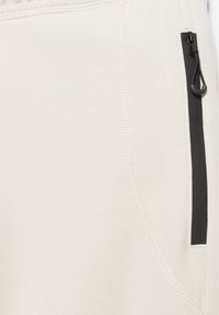 Close-up of beige fabric with visible stitching and a vertical black zipper pocket with a black pull cord.