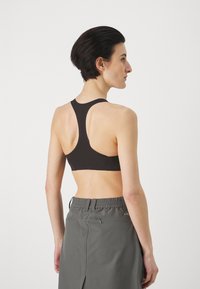 Svart sportsbh med racerback-design, vist fra siden, kombinert med grå, elastiske shorts som har en elastisk midje.