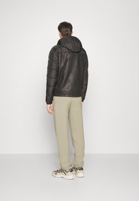 Svart pufferjacka med huva och matt yta, i kombination med ljusbeige joggers och beiga sneakers, sedd bakifrån.