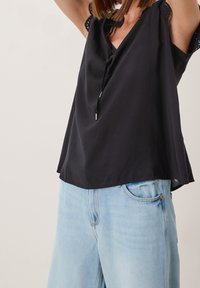 Top nero senza maniche con scollo a V, lacci e dettagli in pizzo. Abbinato a jeans in denim azzurro chiaro con design classico a cinque tasche.