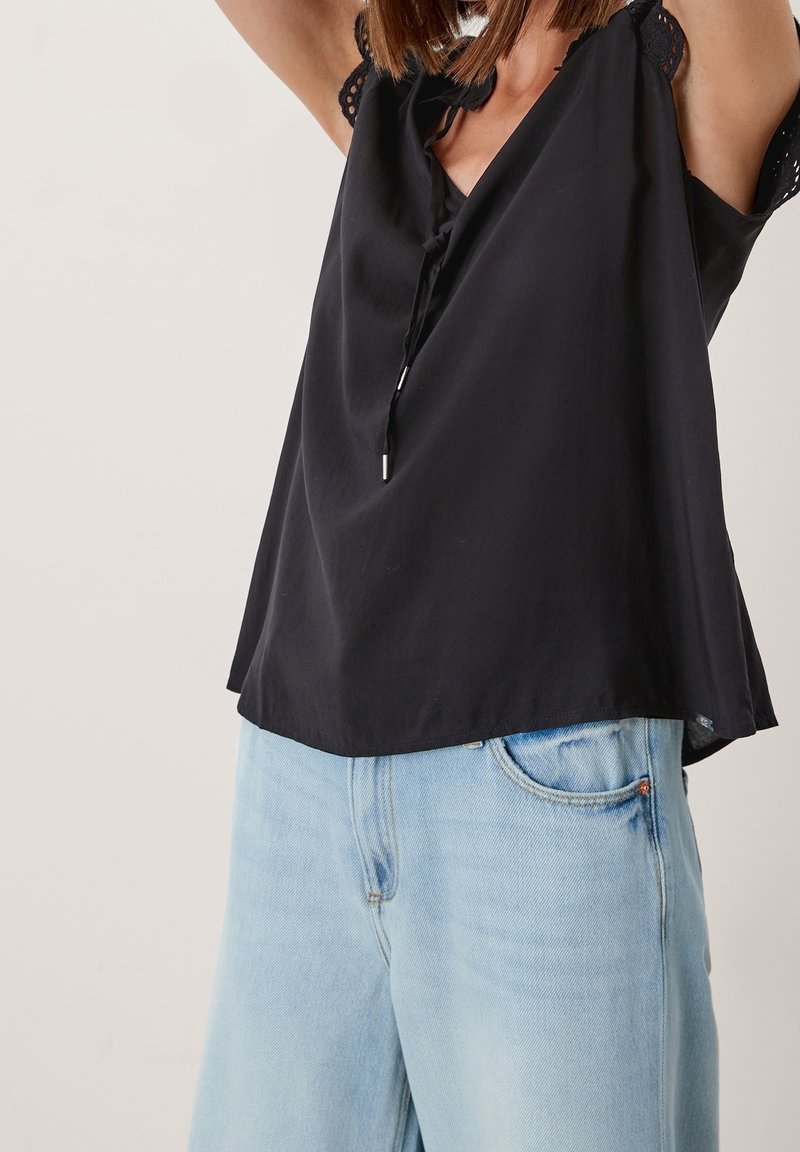 Top nero senza maniche con scollo a V, lacci e dettagli in pizzo. Abbinato a jeans in denim azzurro chiaro con design classico a cinque tasche.