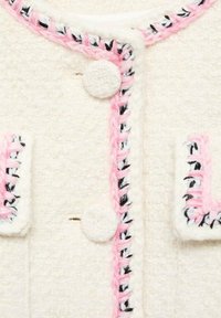 Biała teksturowana tkanina z różowymi i czarnymi plecionymi akcentami, okrągłymi guzikami i obszytymi krawędziami wokół kieszeni i kołnierza.