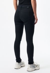 Černé skinny džíny s vysokým pasem, hladkým povrchem, zadními kapsami a kombinované se světlými sportovními botami.