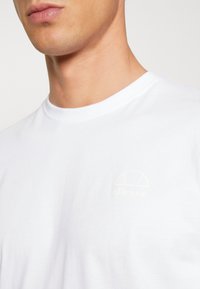 Hvid bomulds T-shirt med et diskret, lysefarvet logo på brystet. Rund halsudskæring og glat tekstur.