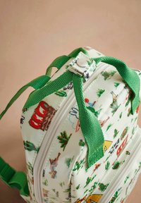 Malý batoh má bílou látku zdobenou barevnými vzory s tématikou kempování, zelenými zipy a pevnými zelenými popruhy na ramena.