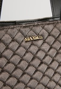 Sac à main en tissu gris matelassé avec une texture lisse, logo doré "MAX&Co" et poignées d'accentuation noires. Présente un motif en losanges sur toute la surface.