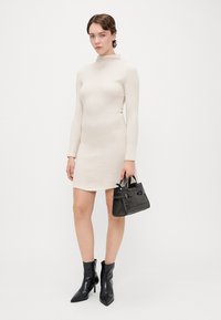 Robe crème à manches longues et côtelée avec un col haut. Associée à des bottes noires à la cheville et un petit sac à main texturé. Silhouette simple et ajustée.