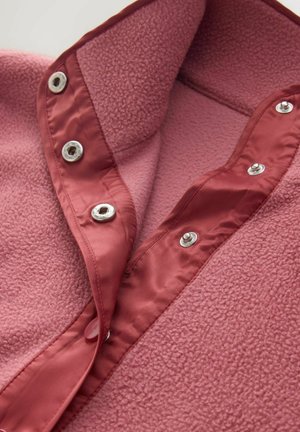 Material de fleece roz cu o margine asemănătoare satinului, cu nasturi tip snap argintii, parțial descheiat pentru a arăta textura și detaliile de închidere.