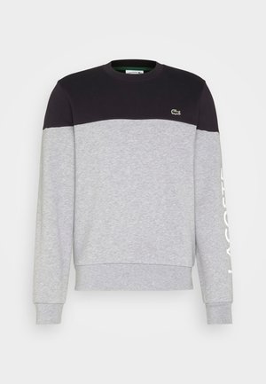 Langärmliges Sweatshirt mit Rundhalsausschnitt, schwarzem Oberteil, hellgrauem Körper und Ärmeln, kleinem grünem Krokodillogo auf der Brust und weißem Text auf dem Ärmel.