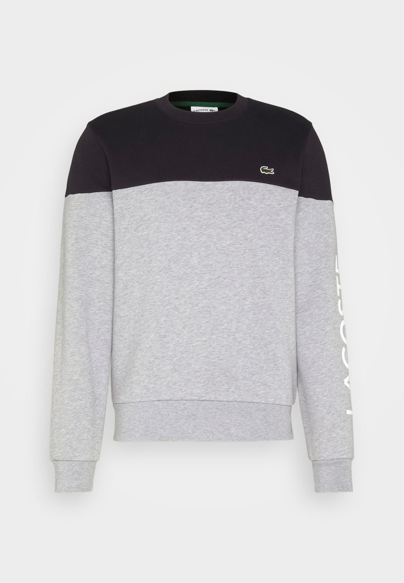 Sweatshirt à manches longues et col rond avec partie supérieure noire, corps et manches gris clair, petit logo crocodile vert sur la poitrine et texte blanc sur la manche.