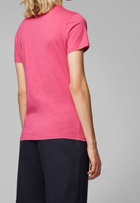 Kortärmad rosa t-shirt i bomull med rundad halsringning och avslappnad passform, kombinerad med mörka byxor. Bakvy visas.