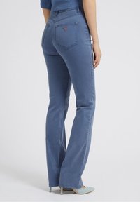 Světle modré denimové zvonové džíny s hladkou texturou, designem se pěti kapsami a malým logem na zadní kapse.