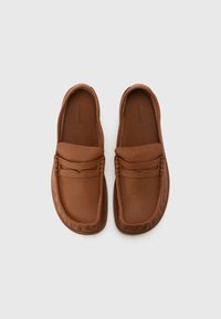 Brūni ādas slip-on apavi ar teksturētu virsmu, ar plašu auduma akcentu pār instepu un smalkām šuvju detaļām.
