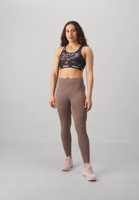 Reggiseno sportivo nero con design grafico e fascia elastica; leggings marroni a coste; scarpe da ginnastica rosa chiaro.