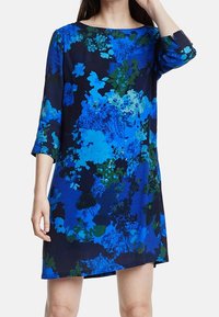 Modré květinové šaty ve stylu shift s 3/4 rukávy, které mají kombinaci tmavě námořnické, tyrkysové a zelené vzory na lehkém materiálu.