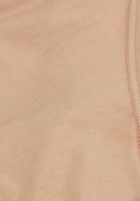 Perzikkleurige stof met een gladde textuur, gekenmerkt door fijne ribbels en een gestikte naaddetail. De close-up benadrukt de zachtheid en rekbaarheid.