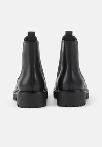 Paire de bottines Chelsea en cuir noir avec semelles à gros crampons, panneaux latéraux élastiques et languettes, vues de dos.