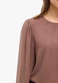 Blusa in chiffon marrone con dettagli delle maniche arricciate e scollatura rotonda, caratterizzata da una texture liscia e un tessuto fluido.
