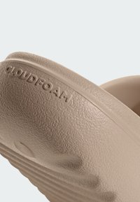 Ljusbeige skumskor utan snörning med texturerad yta, prydda med präglad detalj av "CLOUDFOAM", samt en böjd, räfflad sula för bättre grepp.