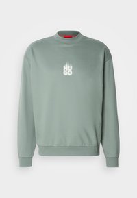 Sweat-shirt vert clair col rond à manches longues avec logo blanc "HUGO" et motif flamme sur la poitrine.