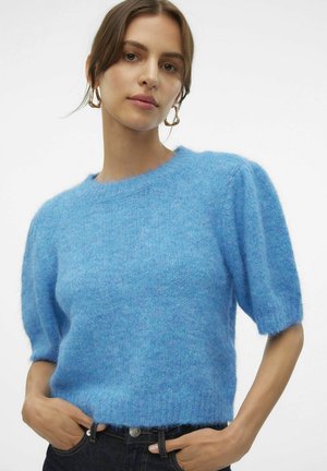 Maglione lavorato a maglia di un blu chiaro, morbido e soffice, con maniche a palloncino corte e un collo rotondo, presenta un tessuto morbido e testurizzato. Abbinato a jeans scuri.
