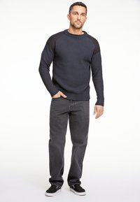 Dunkel gerippter Pullover mit Raglanärmeln, kombiniert mit dunklen Jeans und schwarzen Sneakers. Der Pullover hat eine strukturierte Stoffqualität und einen runden Ausschnitt.