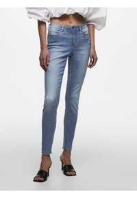 Jeans ajustados de color azul claro con una textura deslavada, ligero desgaste en el muslo y un diseño de cinco bolsillos. Combinados con tacones negros de punta abierta.