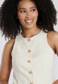 Beige sleeveless top with a round neckline, featuring five decorative gold-tone buttons along the front, crafted from textured fabric.