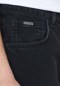 Černé džínové kalhoty z denimu s detaily předních kapes, vybavené kovovou nášivkou "PEGADOR" a viditelným šitím podél švů.