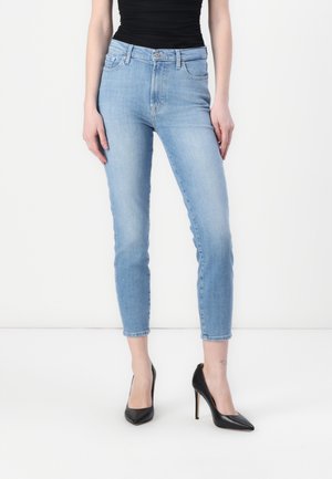 Lichtblauwe skinny jeans met een hoge taille, subtiele vervaging en gestikte zakken, gecombineerd met zwarte hoge hakken.