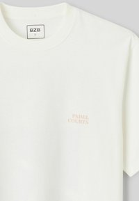 T-shirt en coton blanc avec col rond et manches courtes. "PADEL COURTS" imprimé en rose sur la partie supérieure gauche de la poitrine.