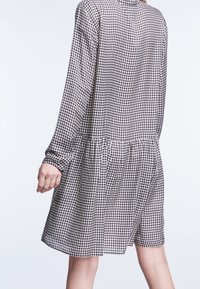 Langarm jurk in zwart-wit houndstoothpatroon, met een geplooide taille en een ontspannen silhouet. Zachte stof met een gladde textuur.