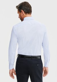 Jasnoniebieska koszula z długim rękawem z kołnierzykiem zapinanym na guziki, połączona z ciemnymi spodniami i czarnym paskiem. Gładki materiał, dopasowany krój, bez wzorów.